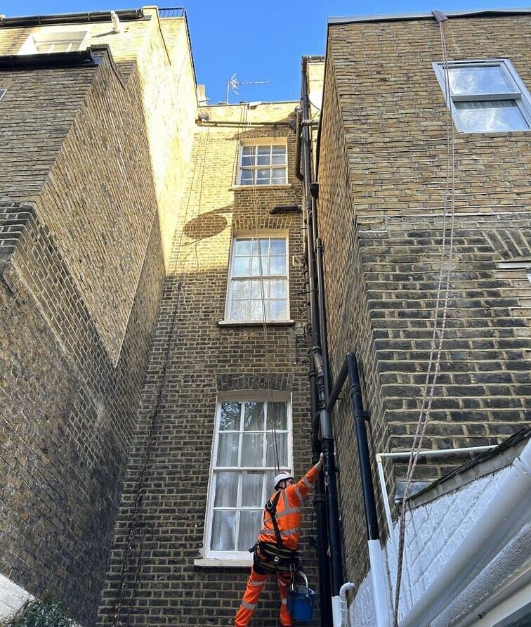 Rope access technician performs rope access painting and decorating on building