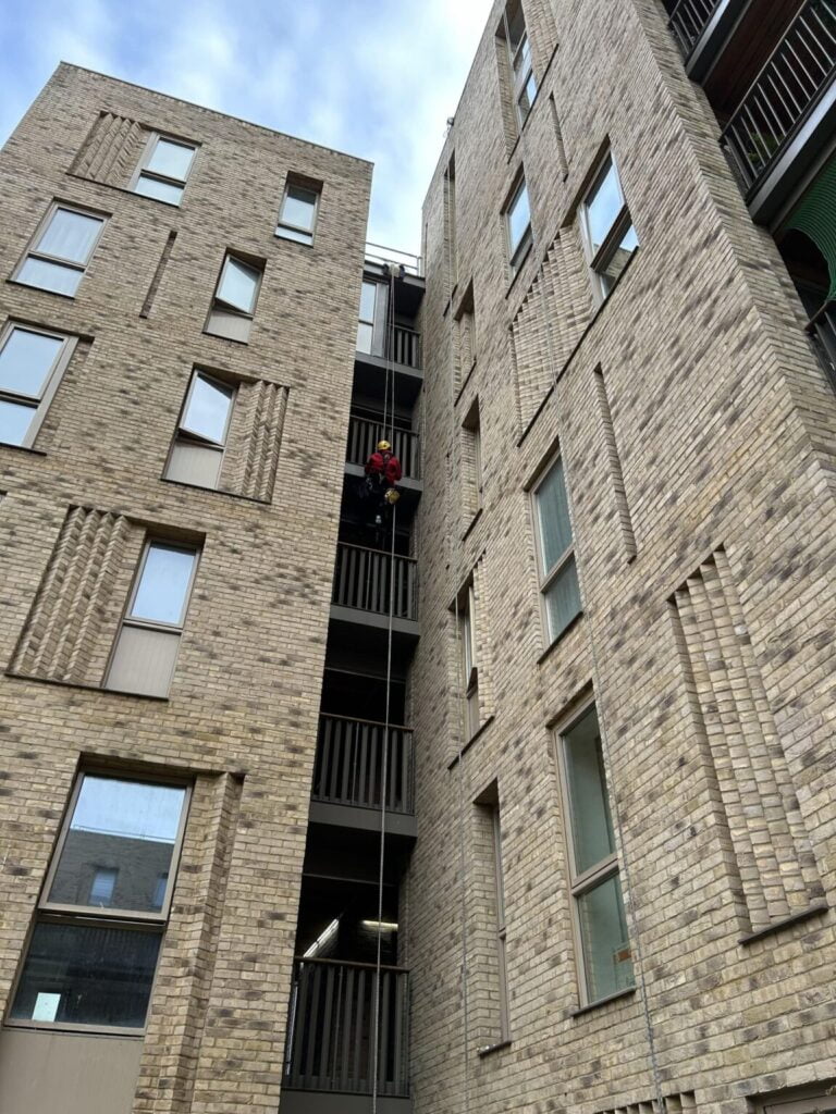 Avisan rope access technician hanging from rope completing brickwork masonry cleaning on tall building