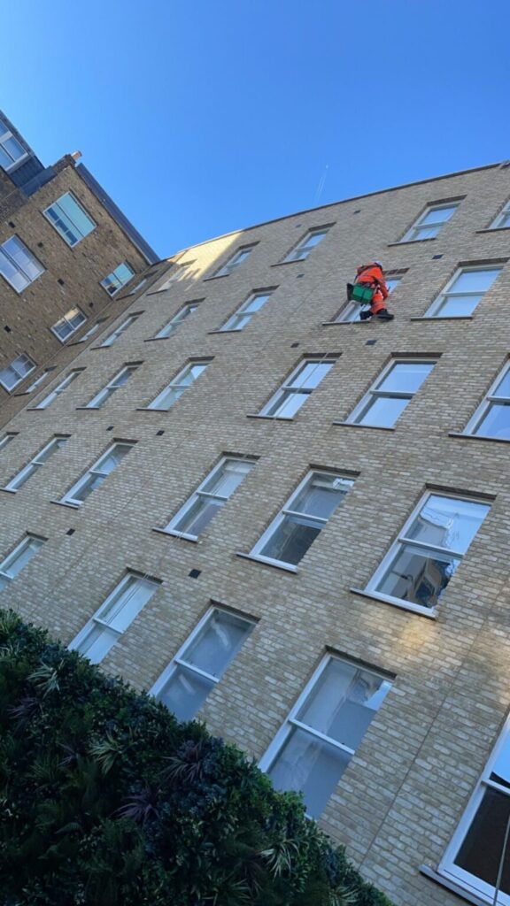 Avisan rope access technician performing high level cleaning on the window of a building