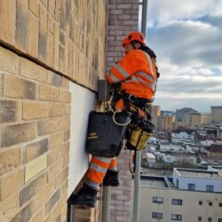 Rope technician from rope access company Avisan hanging by rope on exterior of tall building carrying out repairs