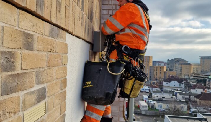 Rope technician from rope access company Avisan hanging by rope on exterior of tall building carrying out repairs