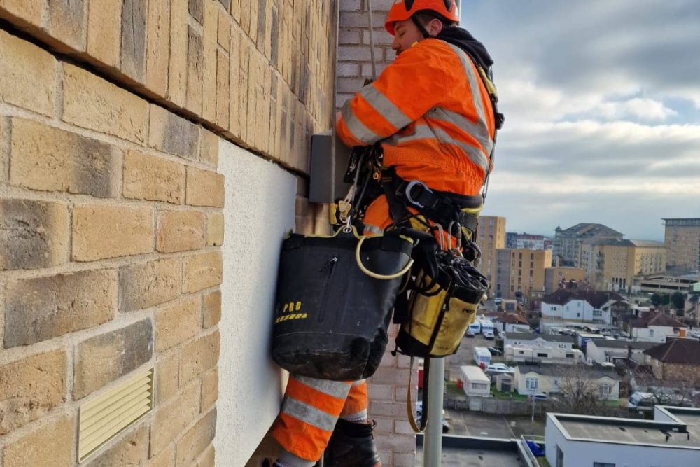 Rope technician from rope access company Avisan hanging by rope on exterior of tall building carrying out repairs